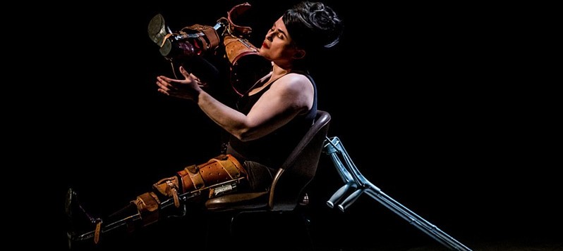 Produktionsbild Une Bouche. Frau sitzt auf Stuhl mit Krücken und Beinschienen.