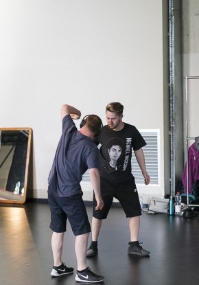 Zwei junge Männer in dunkler Kleidung bewegen sich als Spiegelbild voneinander.