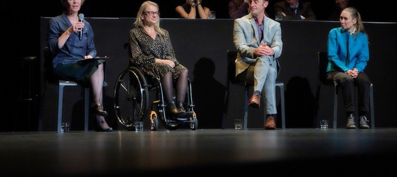 Vier Mitarbeitende von BewegGrund sitzen nebeneinander während der Preisverleihung. Susanne Schneider spricht in ein Mikrofon. Neben ihr sitzt Cornelia Jungo im Rollstuhl, weiter rechts folgen Jürg Koch und Esther Kunz.