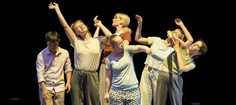 Bühnenaufnahme des Stückes Milles Sens. Sechs unterschiedliche Jugendliche stehen als lose Gruppe beisammen. Gebadet in warmes Licht strecken, wenden und ranken sie ihre Oberkörper und Arme