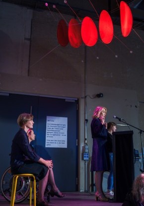 Eröffnungsansprache der Stadtpräsidentin Marieke Kruit am Rednerpult.  Sie steht an einem Rednerpult.  An der Decke hängt eine leuchtend rote Installation.