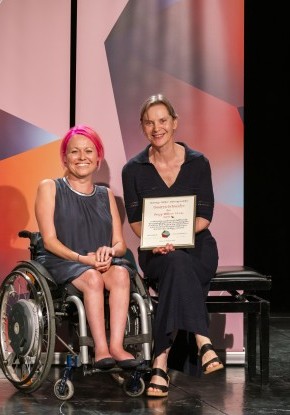 Mirjam Gasser (im Rollstuhl) und Susanne Schneider sitzen nebeneinander und halten gemeinsam die Urkunde des Bürgi-Willert-Stiftung Preises.