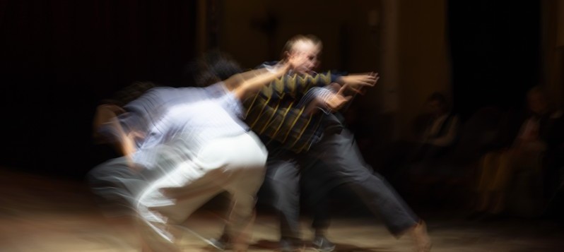 Drei Personen in Bewegung, verschwommen durch lange Belichtungszeit. Dynamische Körperhaltungen, die Energie und Tanz ausdrücken.