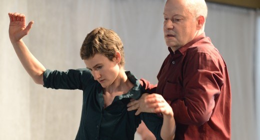 Acht Personen, zwei davon im Rollstuhl sind am Tanzen, ein einziges Licht beleuchtet die Szene.