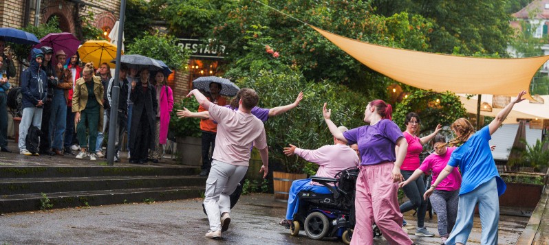 Viele fröhliche, tanzende Menschen mit Rollschuhen oder im Rollstuhl auf der Discofläche. Etwas erhöht steht ein DJ an einem in DJ-Pult. An der Decke strahlt eine Discokugel und im Hintergrund leuchtet in Leuchtschrift "röllele".  